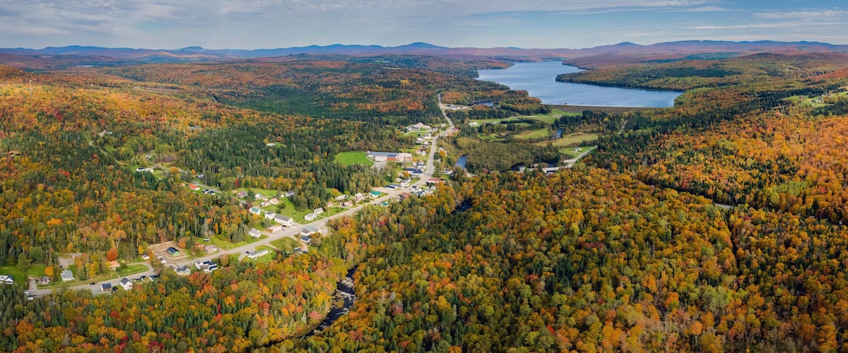 An aerial view of a town nestled in a valley with a lake and mountains in the background.