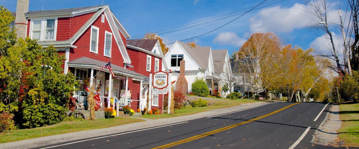A red house with a white porch, a sign for Harman's Cheese, and autumn leaves on the trees.