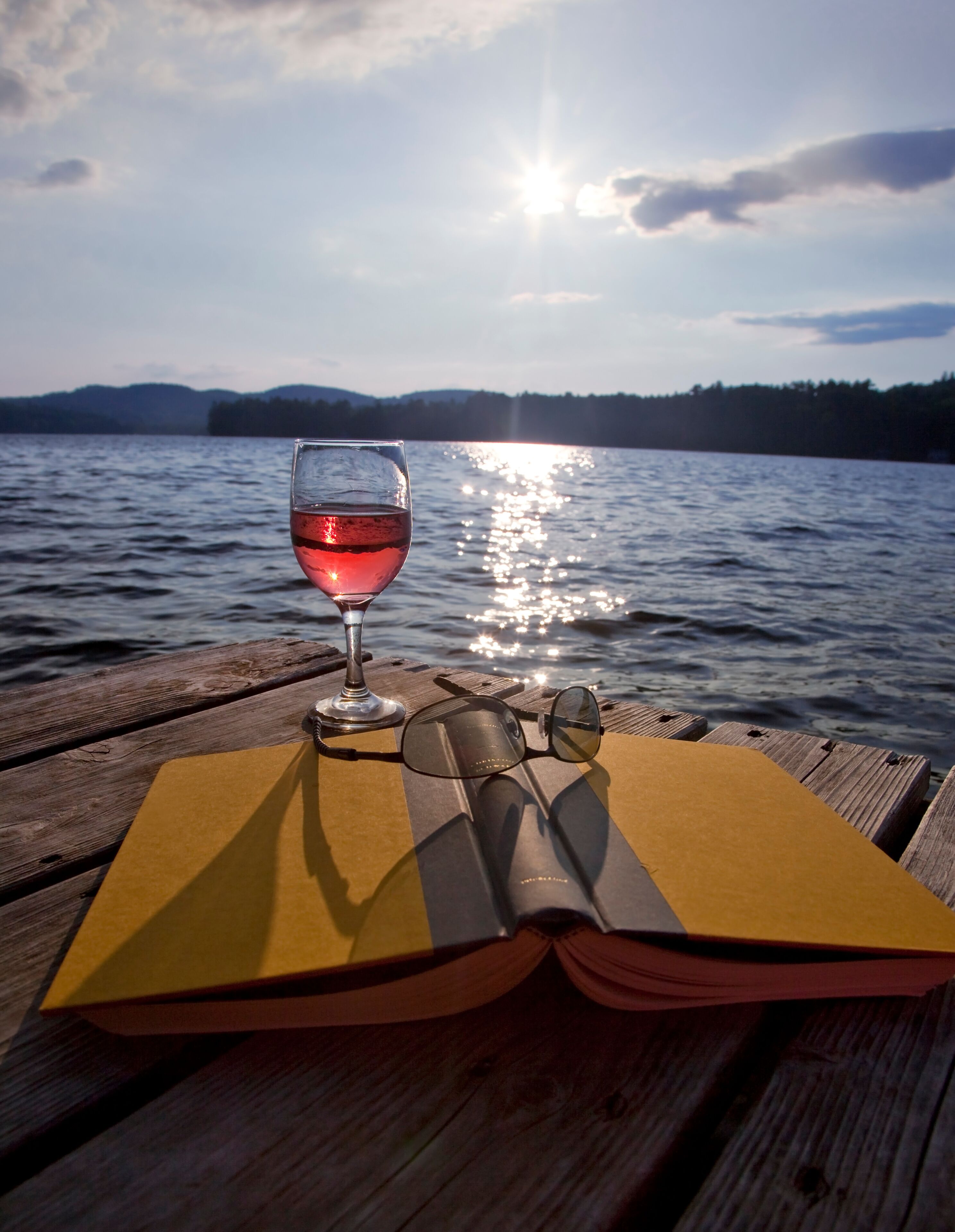 Glass of wine, book, and sunglasses on dock at lake
