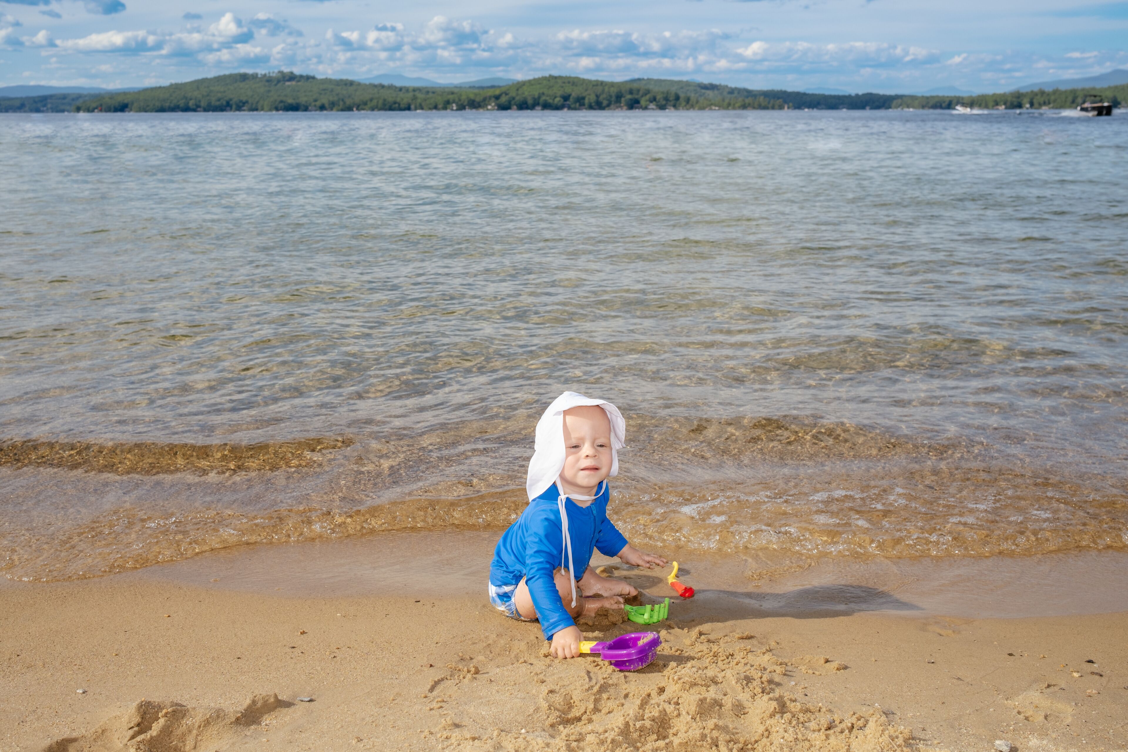 A child playing with sand toys on a beach with a lake and hills in the background.