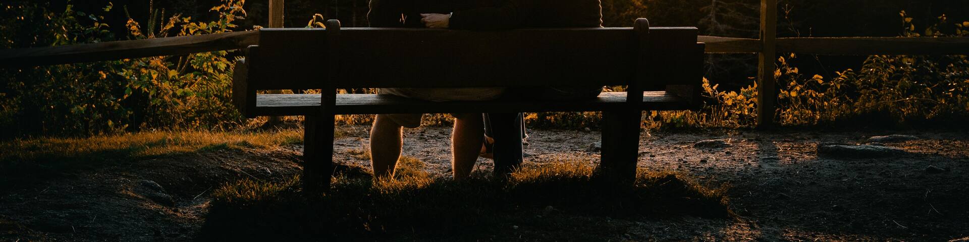 A couple sitting on a bench overlooking a mountainous landscape during sunset.