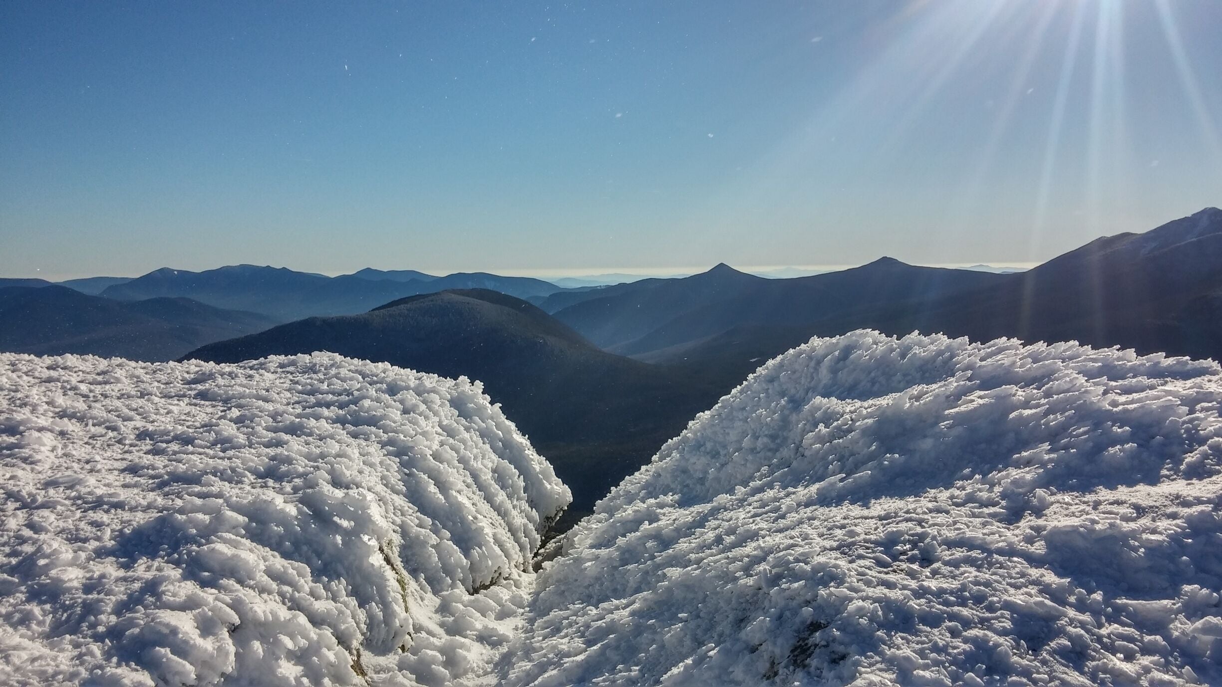 A snow-covered mountain range with a clear sky and sunlight.