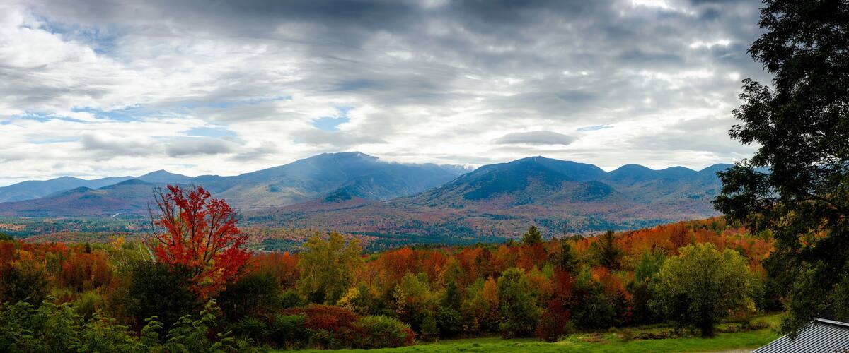 A mountainous landscape with autumn foliage and a cloudy sky.