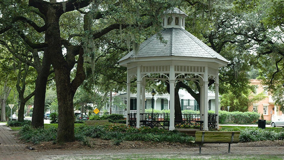 A gazebo surrounded by trees and a bench in a park.
