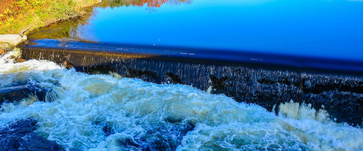 A waterfall with a clear blue pool reflecting autumn foliage.