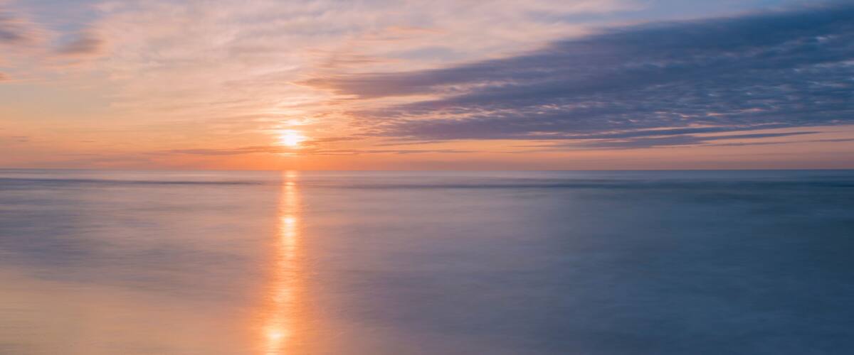 A sunset over a calm sea with a clear sky.