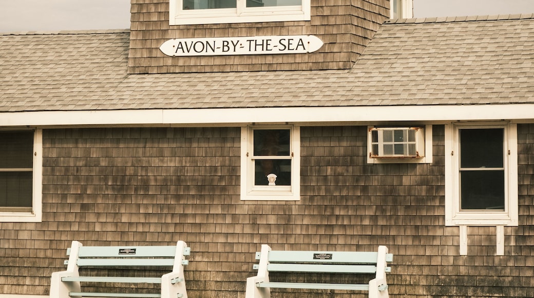 Een houten gebouw met een bord waarop 'AVON-BY-THE-SEA' staat en twee banken ervoor.