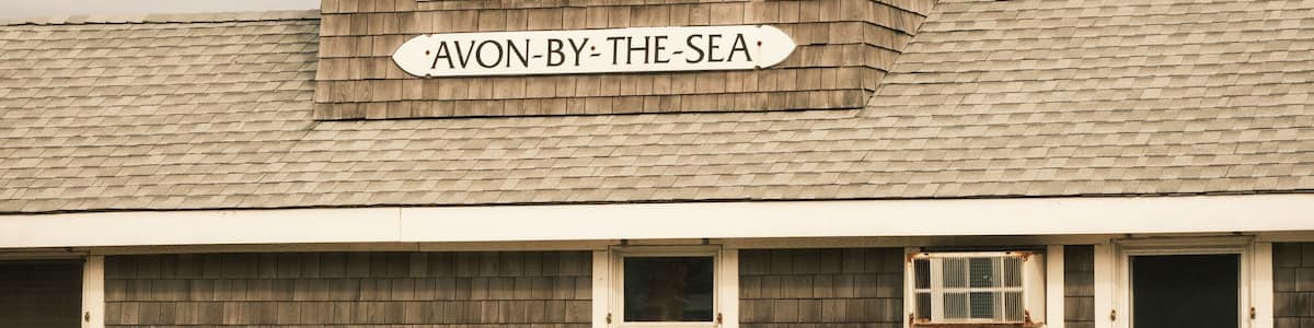 A wooden building with a sign reading 'AVON-BY-THE-SEA' and two benches in front.