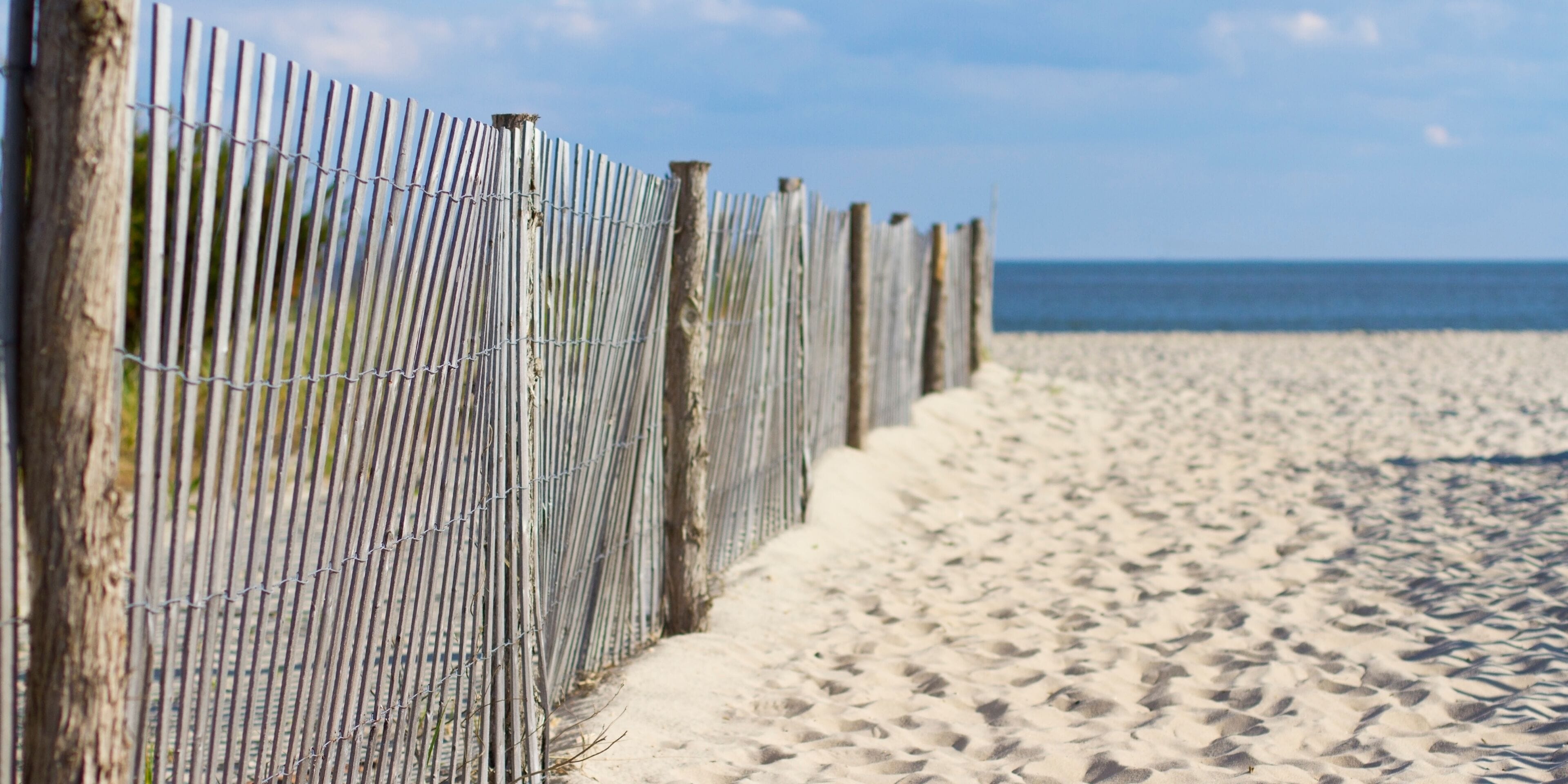 A sandy beach with a wooden fence and a clear blue sky.