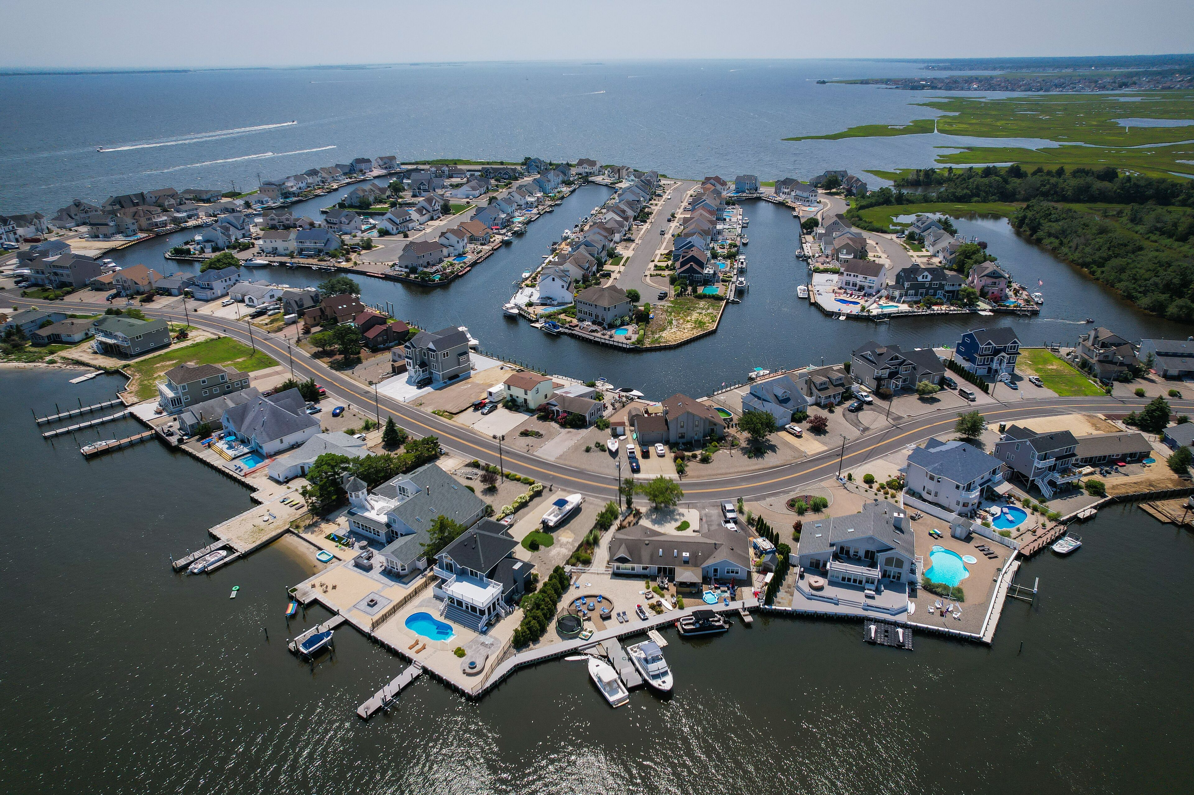 An aerial view of a coastal residential area with houses, docks, and a marina.
