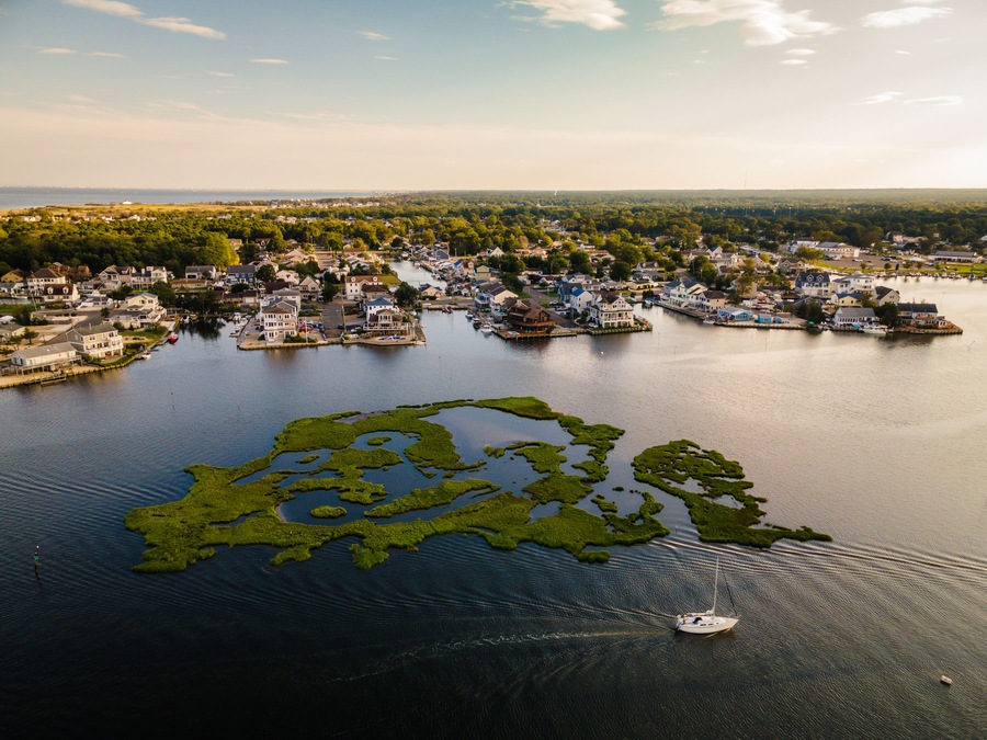 A coastal town with a marina, houses, and a large body of water with green islands.