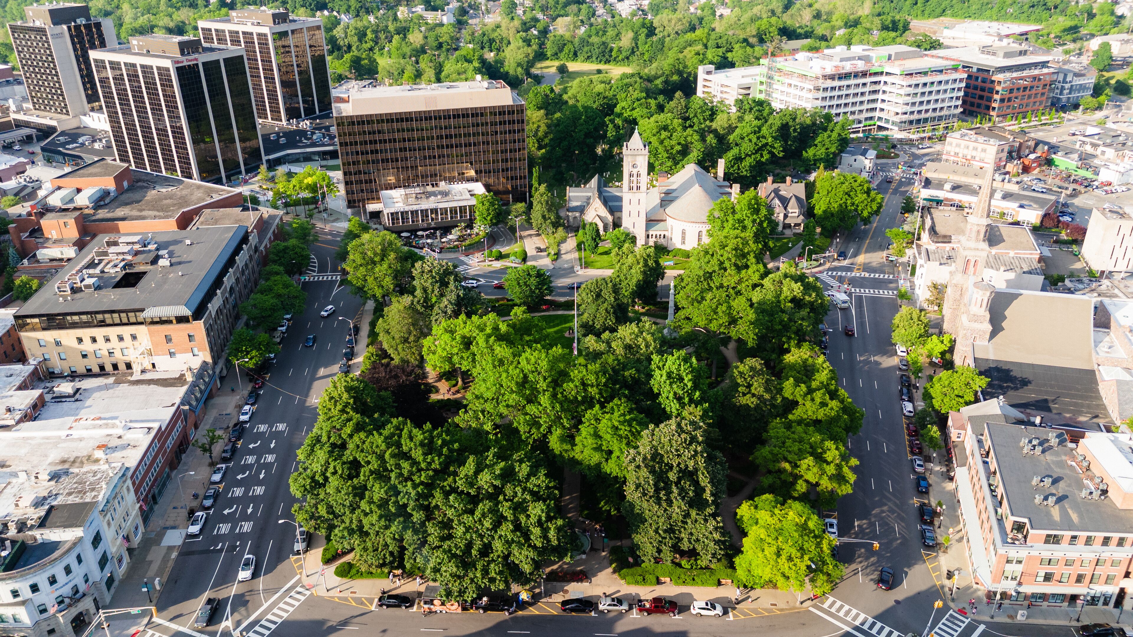 An urban area with a large green park surrounded by buildings, including a church with a steeple.