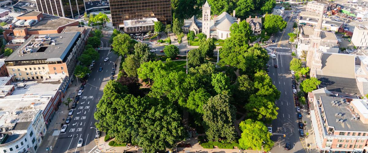 An urban area with a large green park surrounded by buildings, including a church with a steeple.