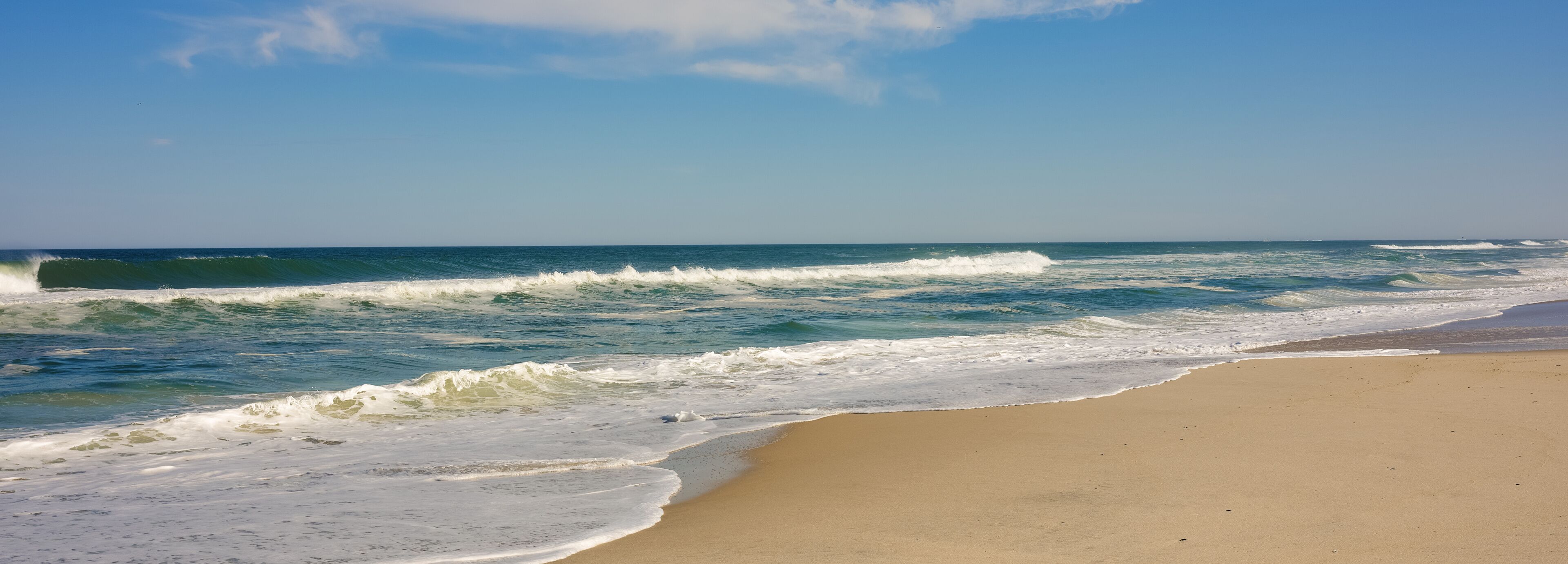 A beach with waves crashing onto the shore under a clear sky.