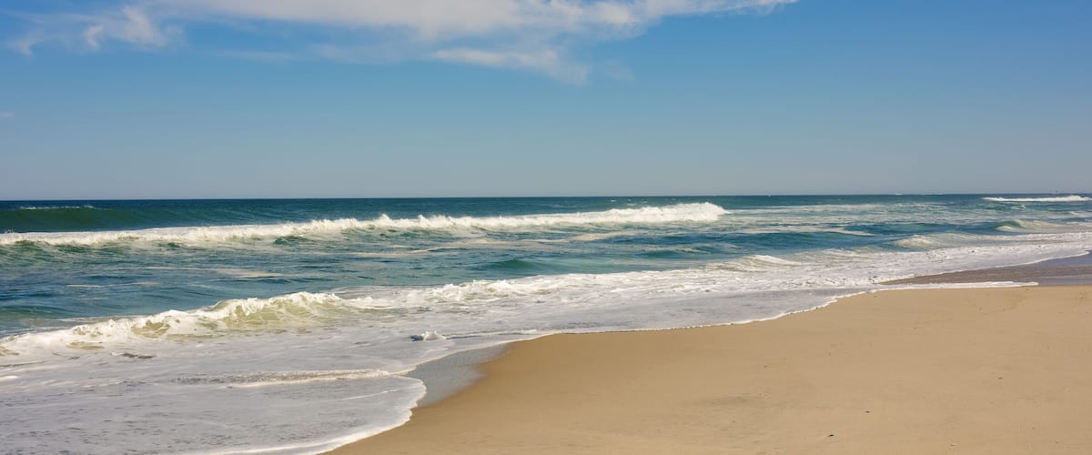 A beach with waves crashing onto the shore under a clear sky.
