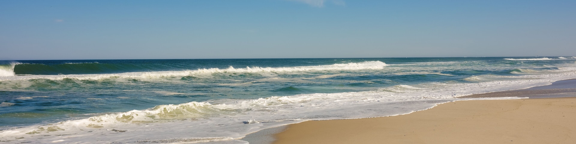 A beach with waves crashing onto the shore under a clear sky.