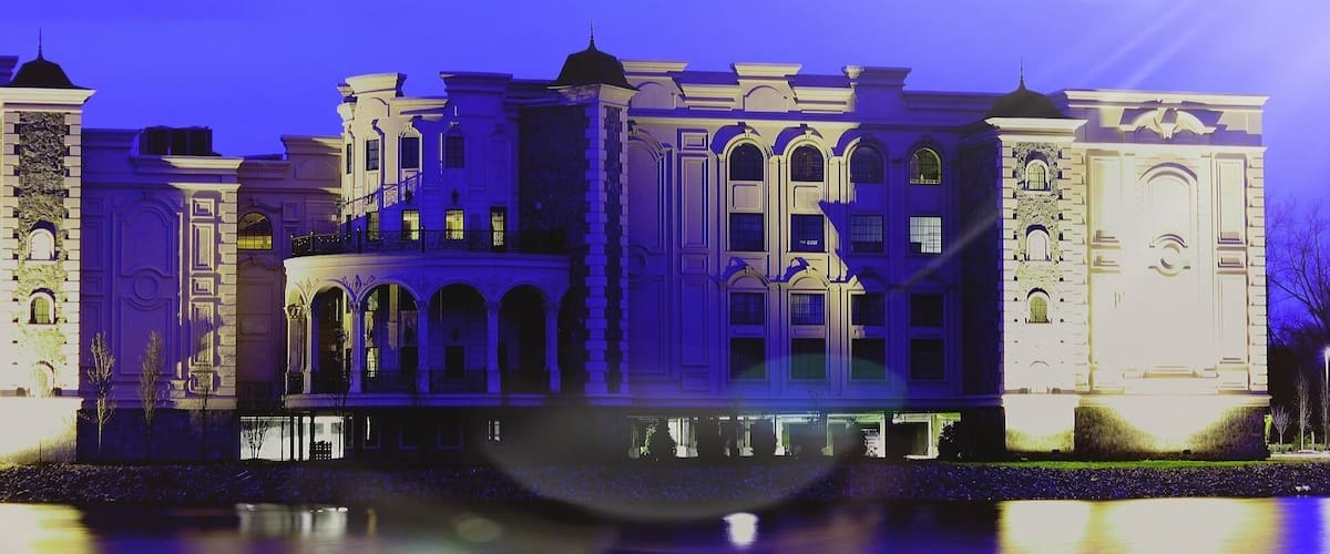A classical building with arched windows and a central courtyard, reflecting on a calm body of water.