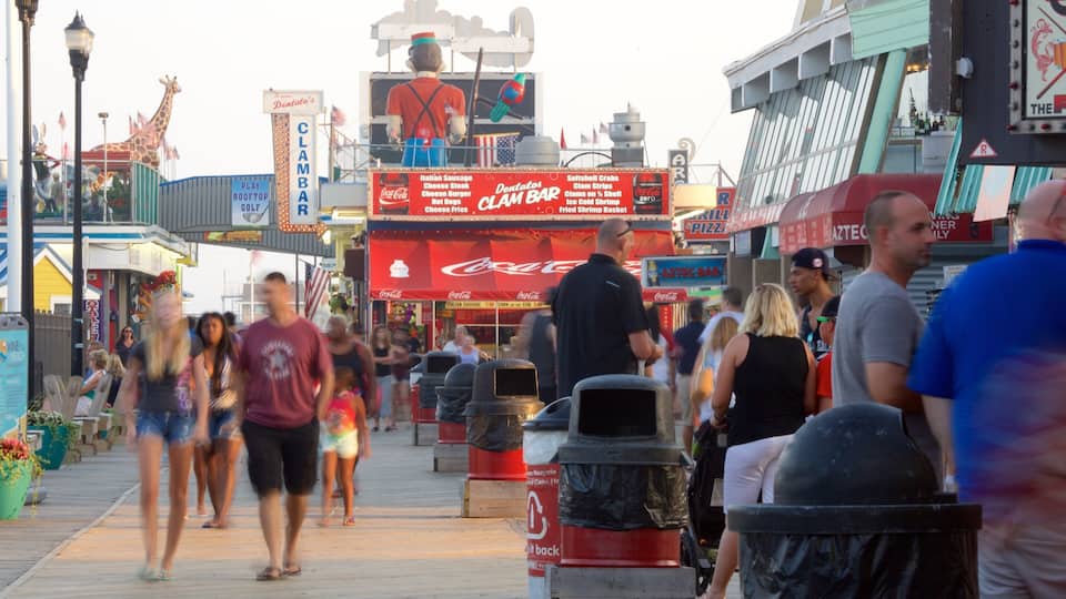 A busy boardwalk with various food stands, including a Coca-Cola stand and a clam bar.