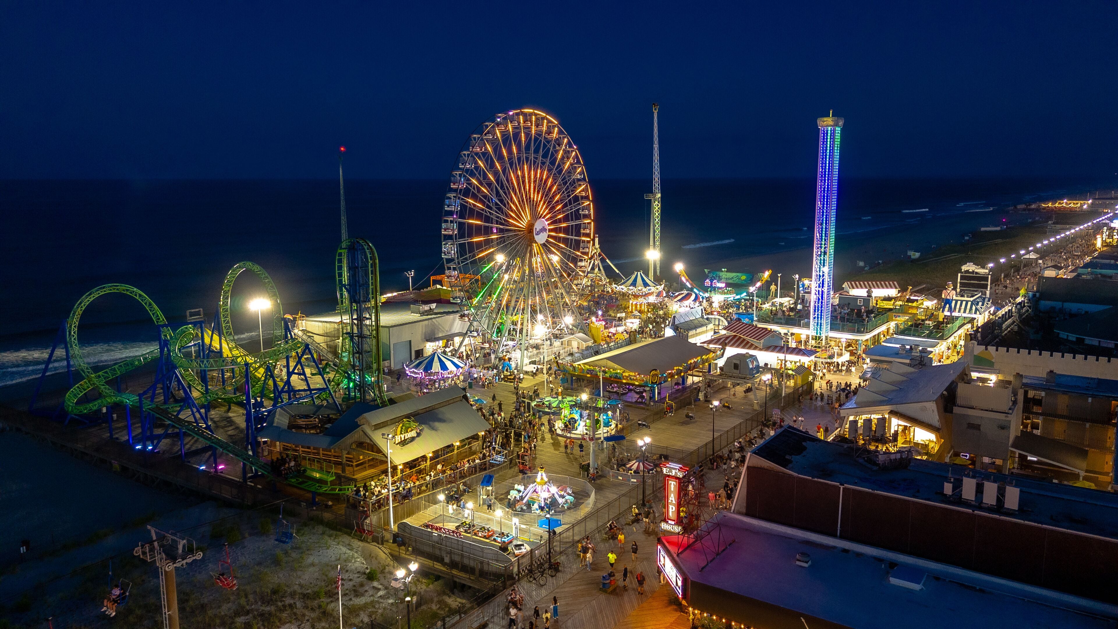 A brightly lit amusement park with a large Ferris wheel, roller coasters, and a tall tower.