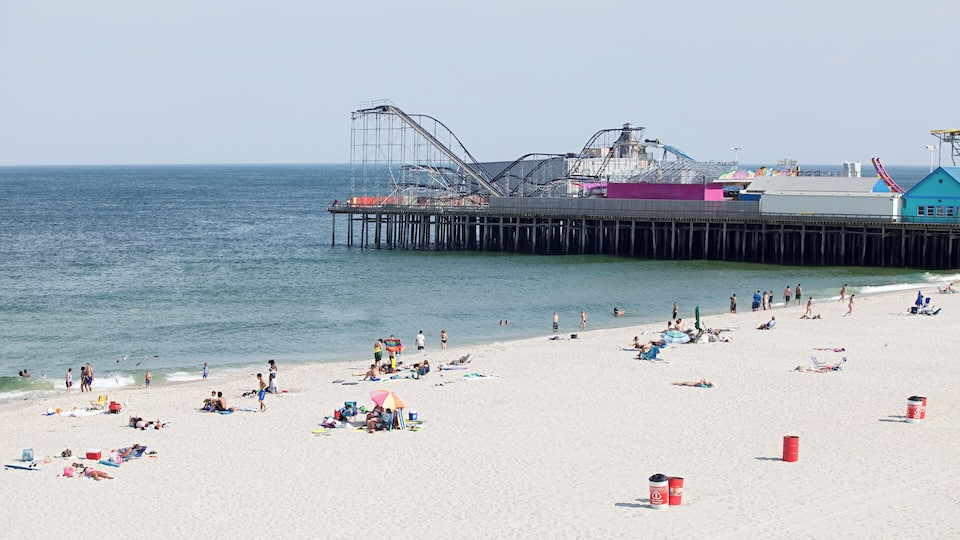 A beach with a pier extending into the ocean, people sunbathing, and beachgoers enjoying the water.