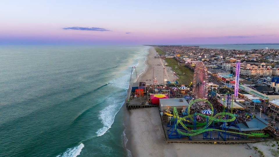 A coastal amusement park with a Ferris wheel, roller coasters, and a beach.