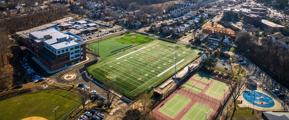 An aerial view of a city with a large football field, tennis courts, and surrounding buildings.