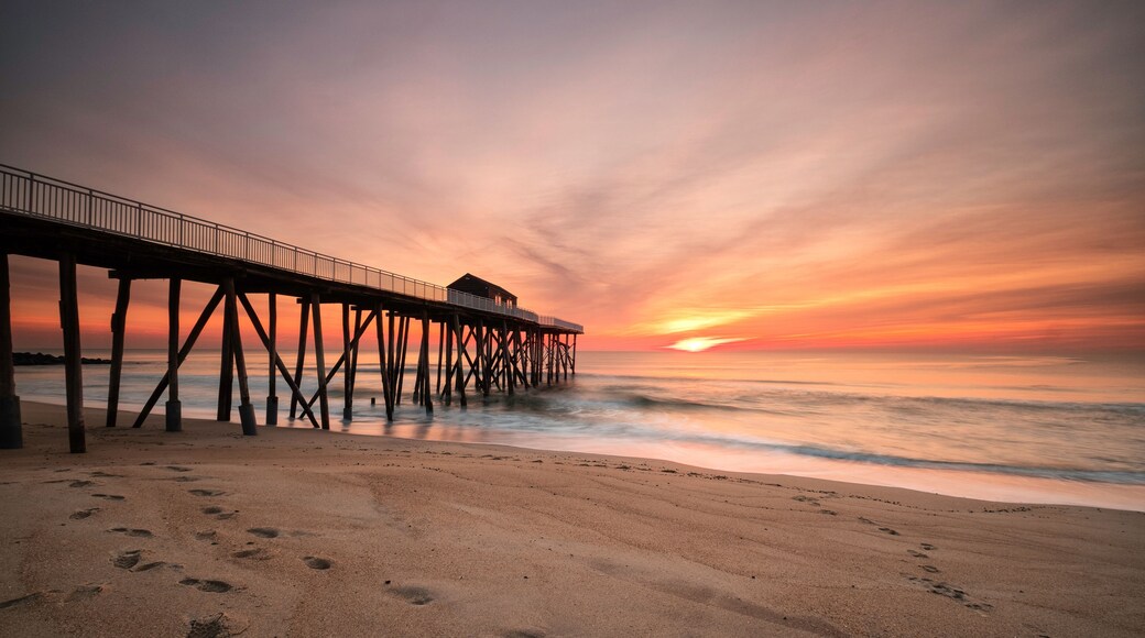 A beach with footprints leading to a pier extending into the ocean.