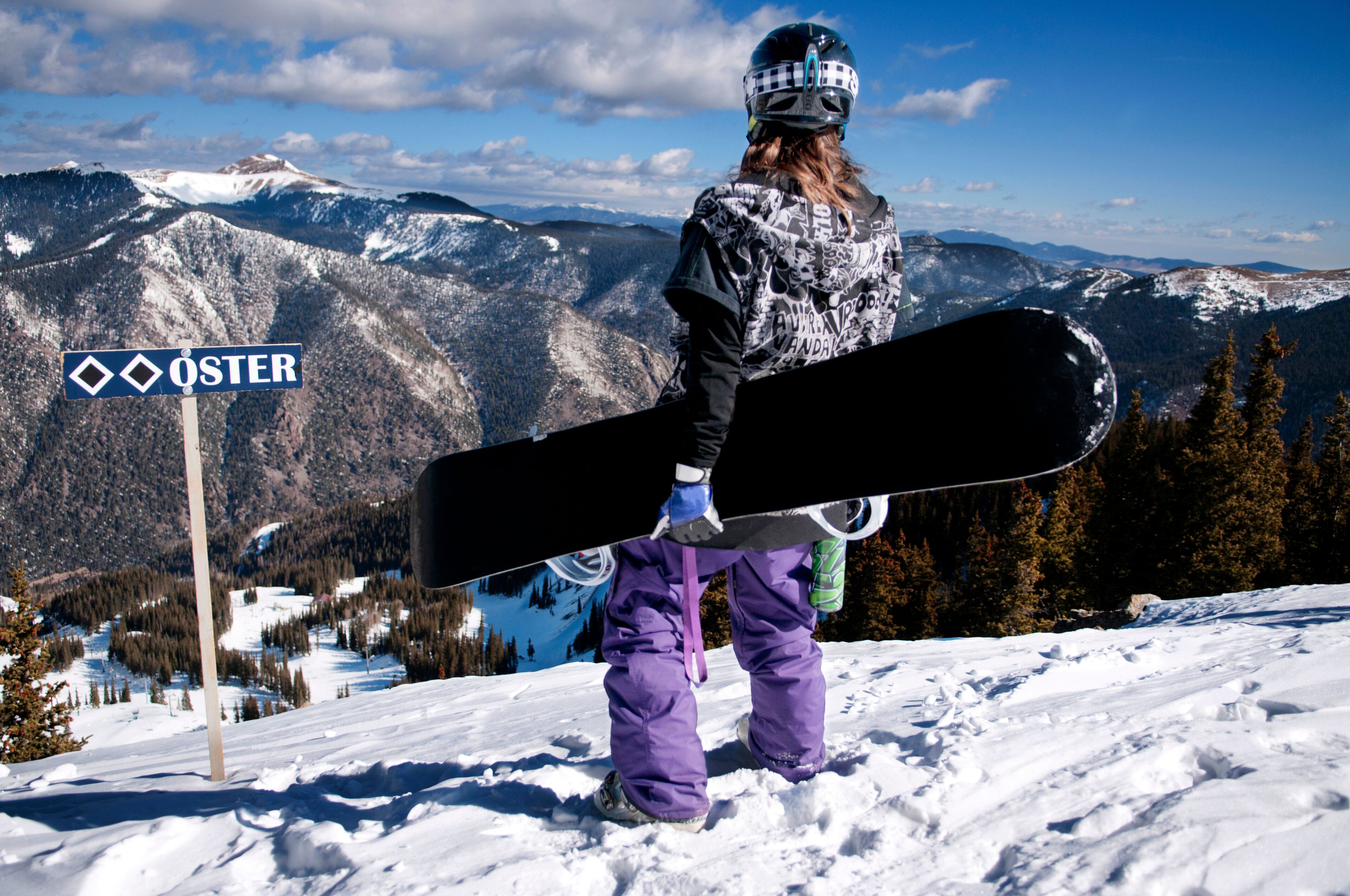 A female snowboarder looks across the mountains on the summit of a double black diamond slope at Taos Ski Valley, New Mexico.