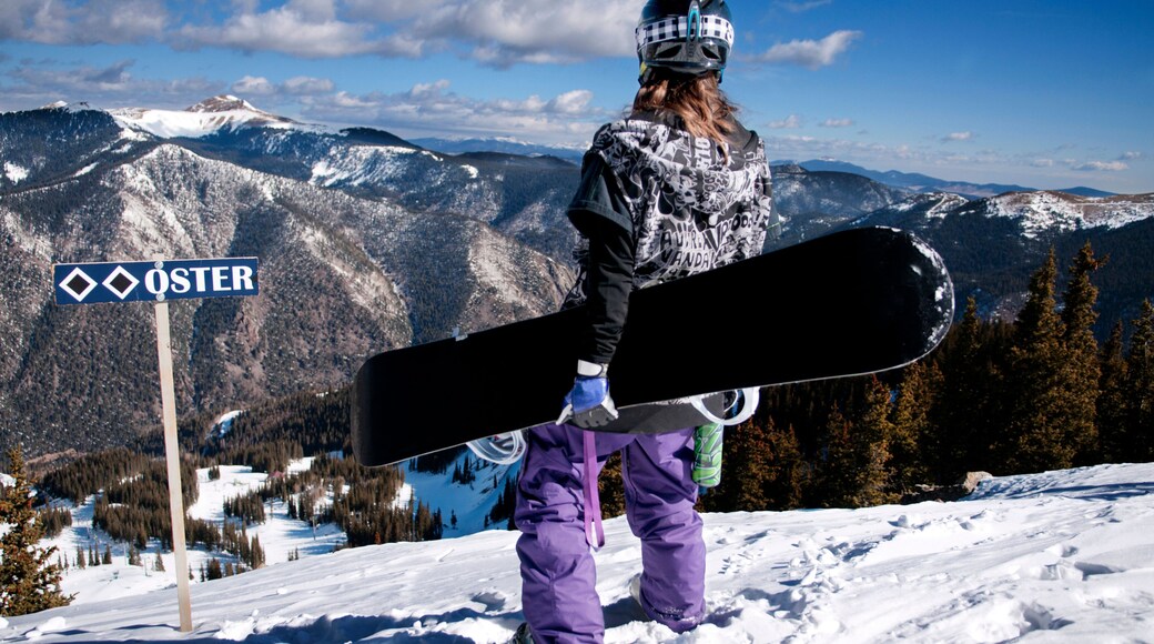 A female snowboarder looks across the mountains on the summit of a double black diamond slope at Taos Ski Valley, New Mexico.