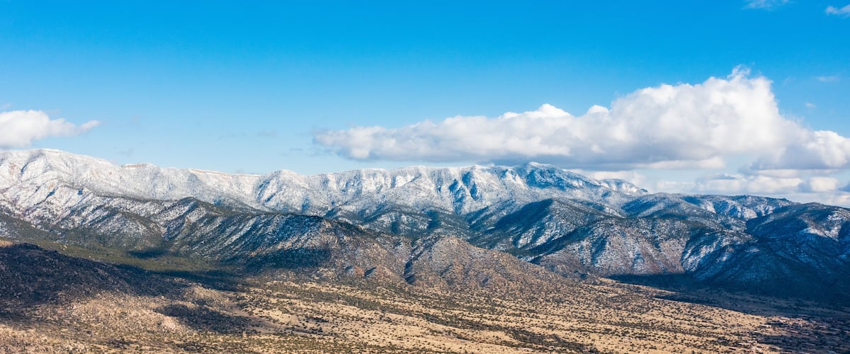 A snow-covered mountain range with a clear blue sky and scattered clouds.