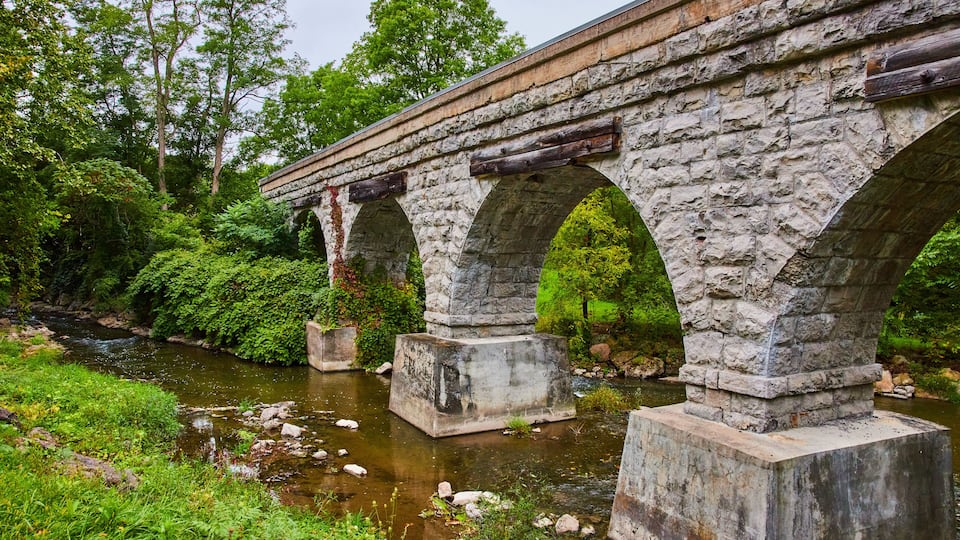 A stone bridge over a river with lush greenery and trees in the background.