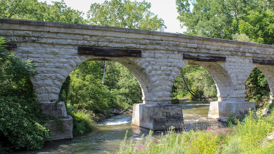 A stone bridge over a river with lush greenery around.