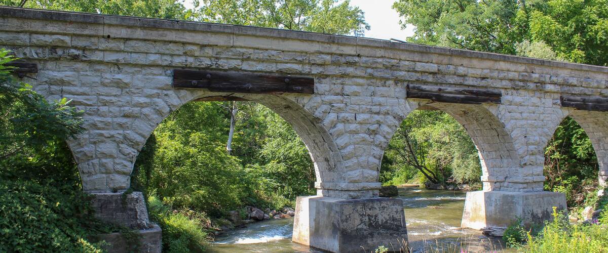 A stone bridge over a river with lush greenery around.