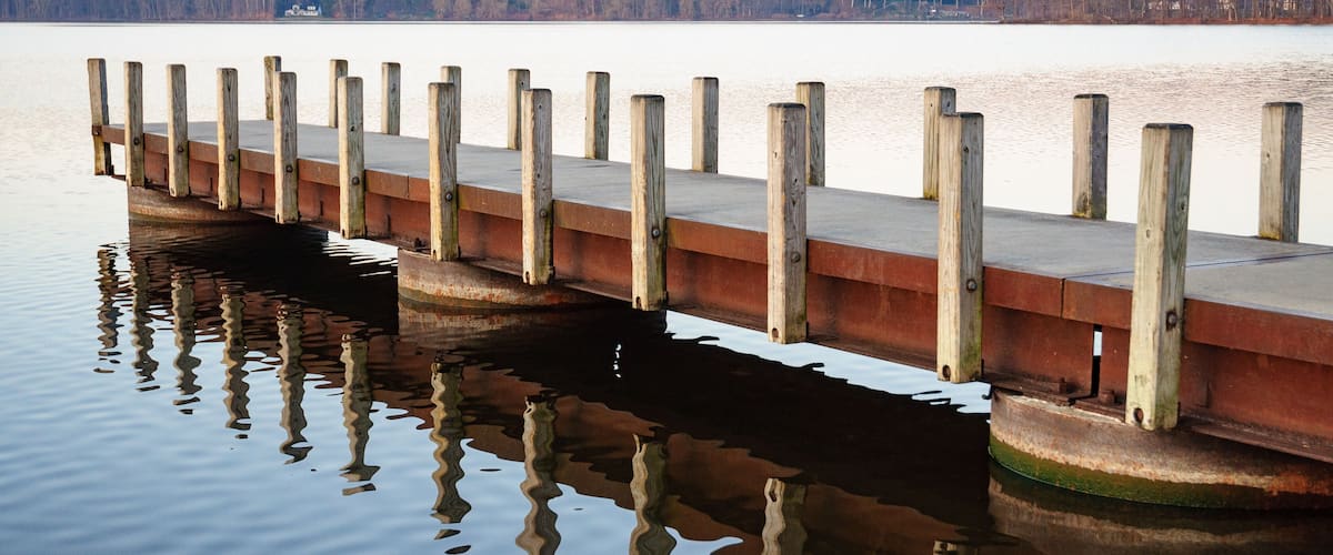 A wooden pier extending into a calm lake with reflections of the pier and surrounding trees.