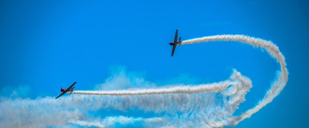 Two airplanes performing aerial maneuvers with smoke trails against a clear blue sky.