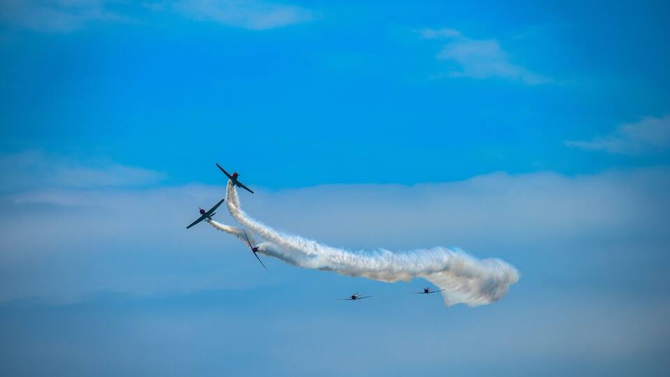 Four airplanes flying in formation with smoke trails against a clear blue sky.
