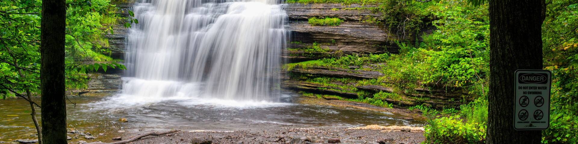 The main cascade at Pixley Falls State Park in Boonville, New York, where water descends over layered shale into a rocky gorge bordered by dense summer forest and moss‑covered ledges