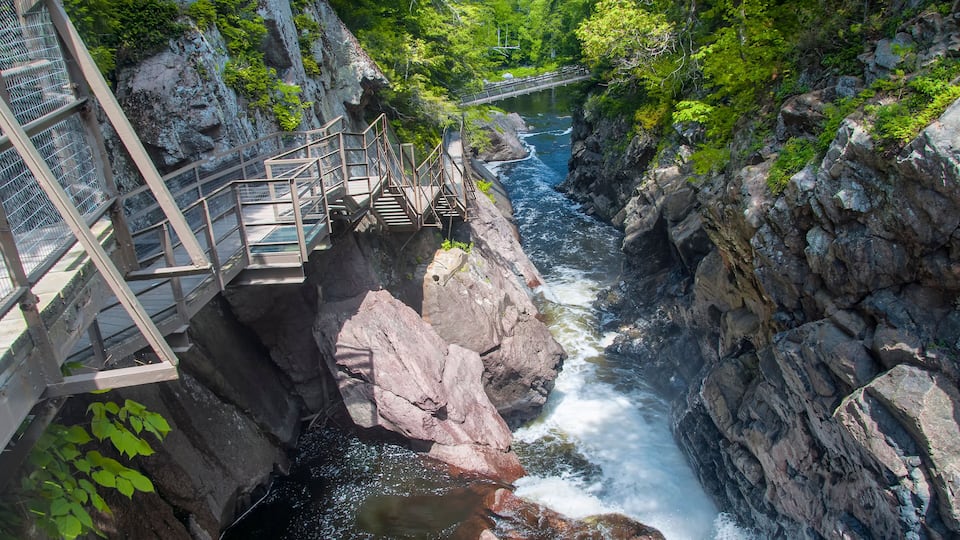 A rocky river gorge with a wooden bridge and metal railing.