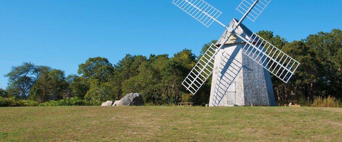 A windmill in a grassy field with trees in the background.
