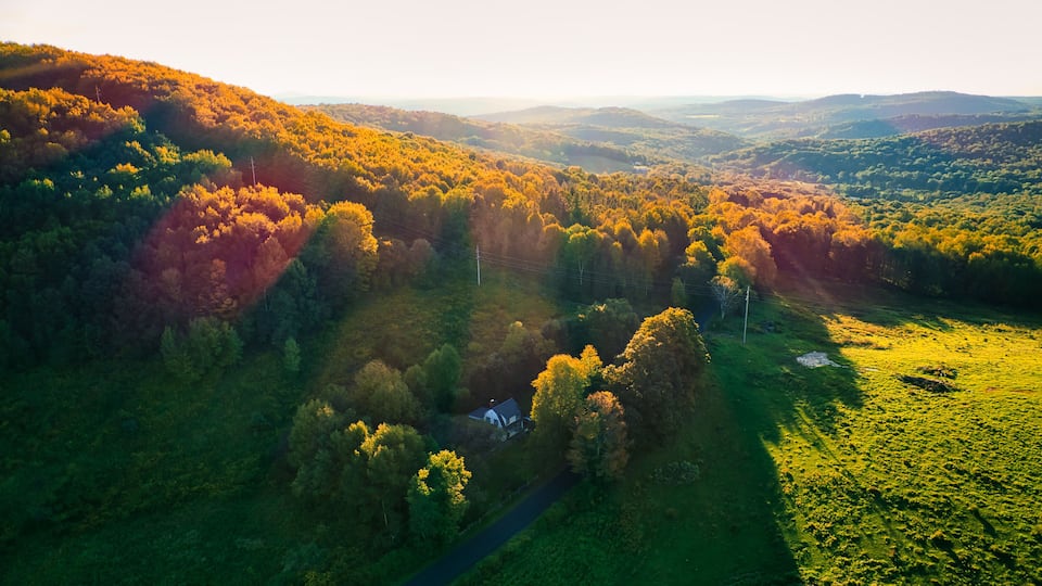 A rural landscape with a house surrounded by autumn-colored trees and rolling hills.