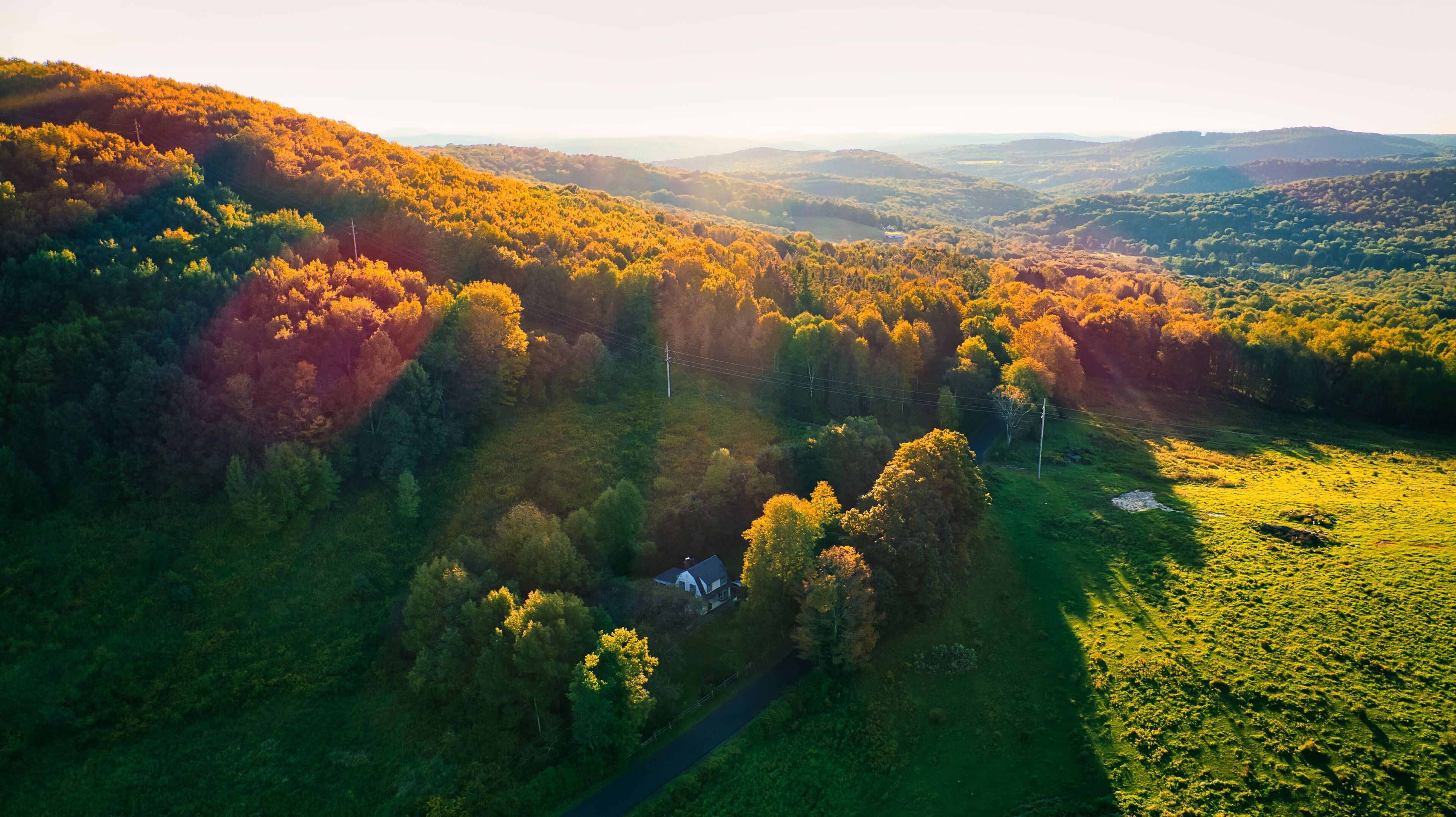 A rural landscape with a house surrounded by autumn-colored trees and rolling hills.