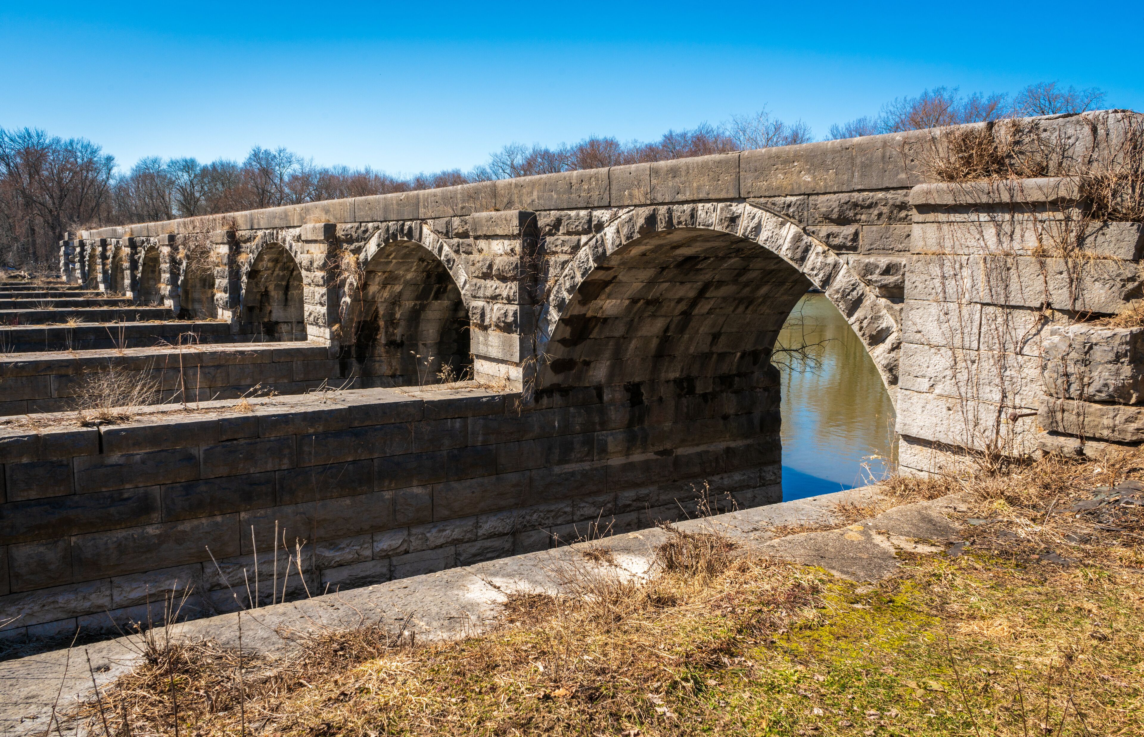 An old stone bridge with multiple arches over a canal.