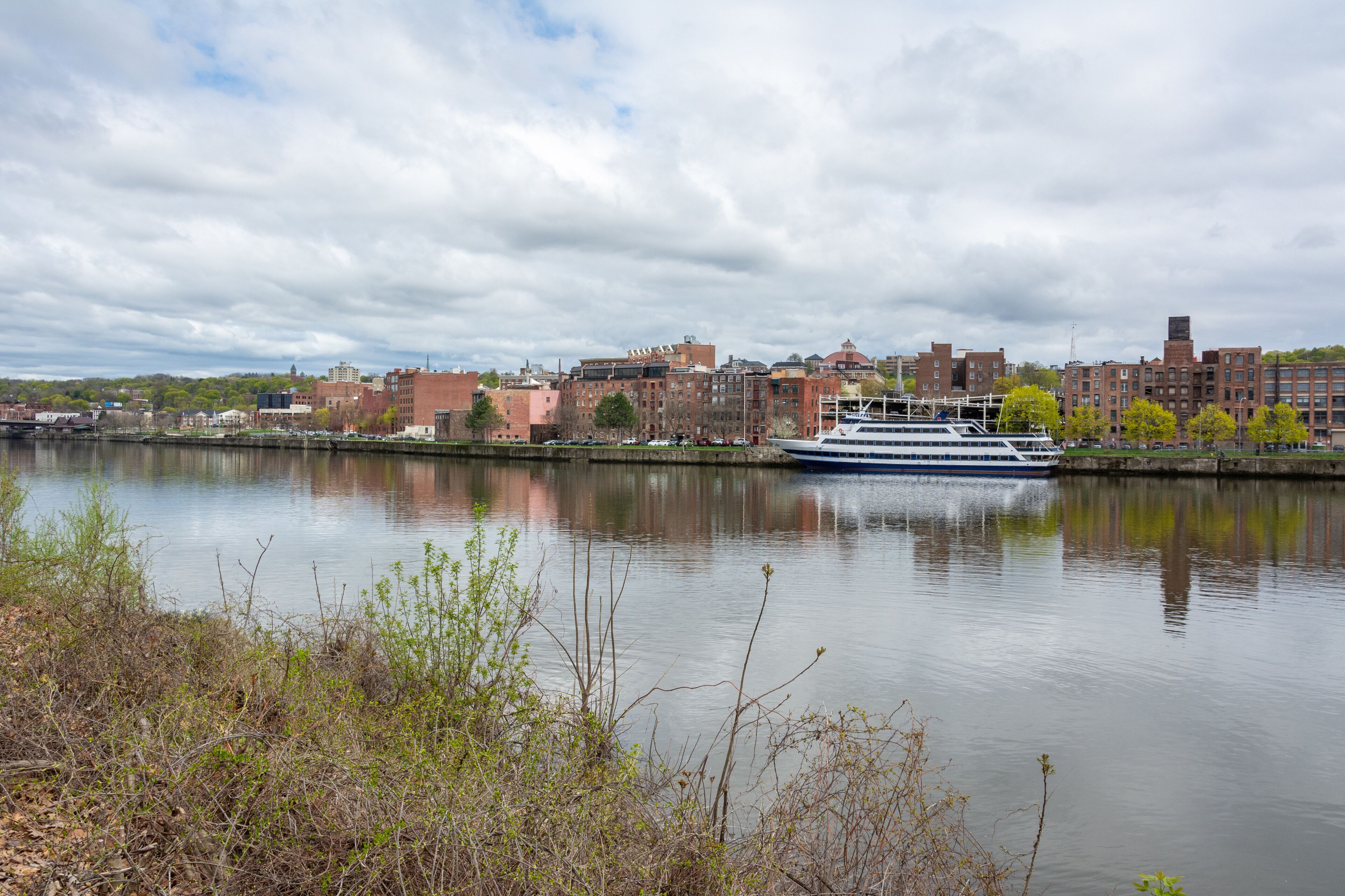 A river with a cruise ship, a city skyline, and a cloudy sky.