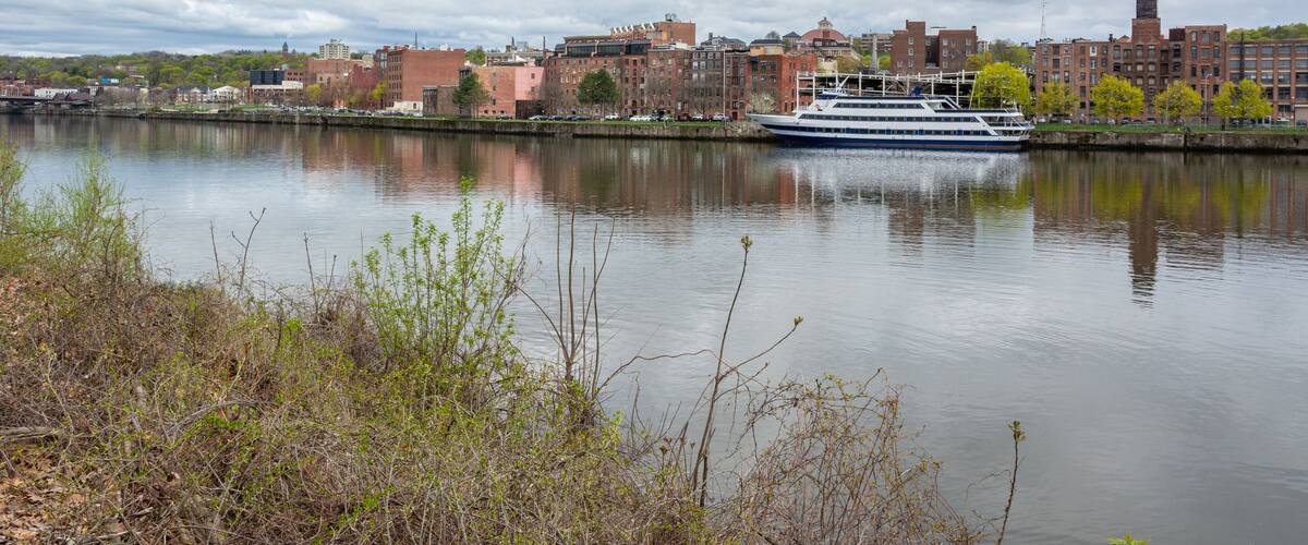 A river with a cruise ship, a city skyline, and a cloudy sky.