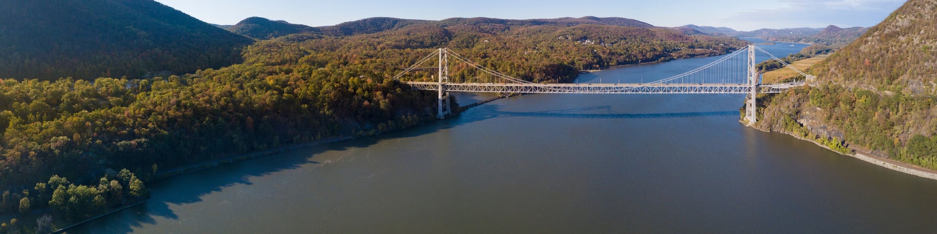 A suspension bridge over a river with surrounding hills and dense forest.