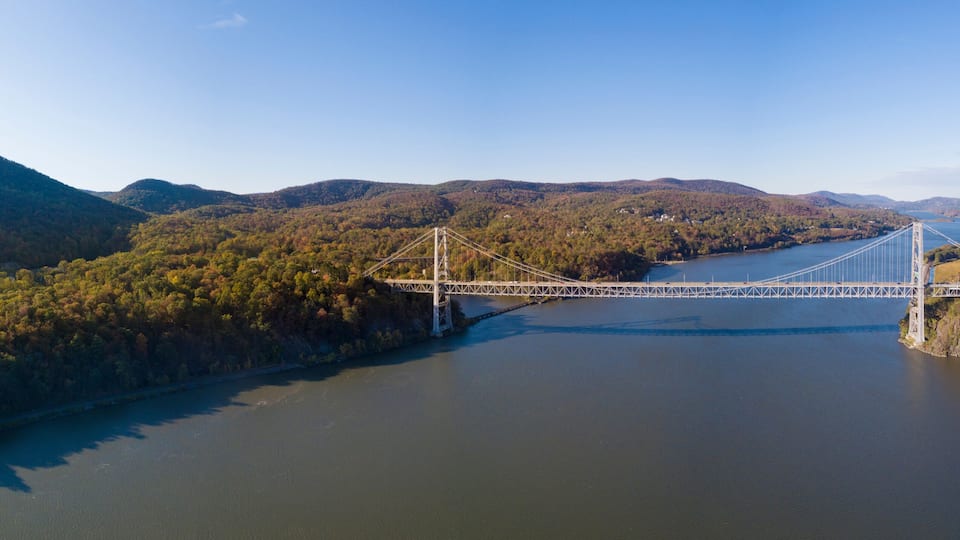 A suspension bridge over a river with surrounding hills and dense forest.