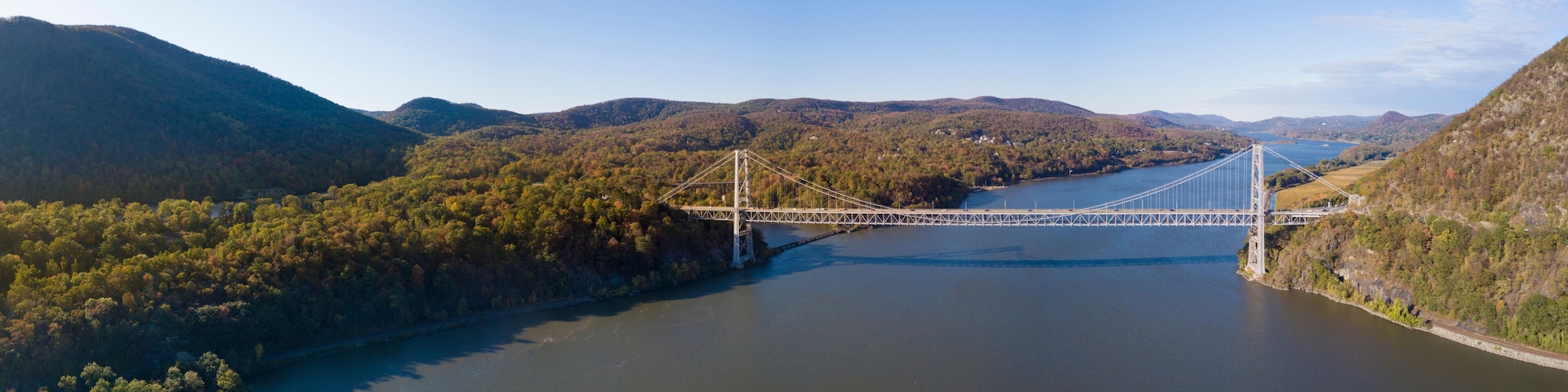 A suspension bridge over a river with surrounding hills and dense forest.