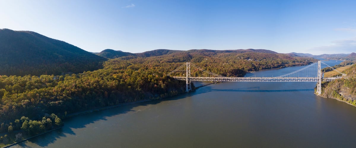 A suspension bridge over a river with surrounding hills and dense forest.