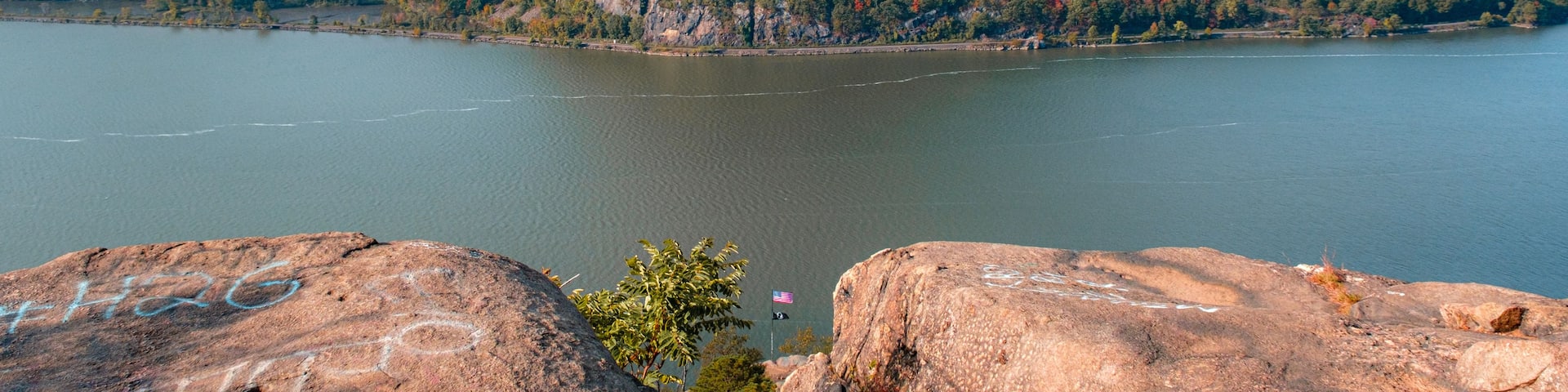 A mountain with a lake in the foreground and a forested hill in the background.