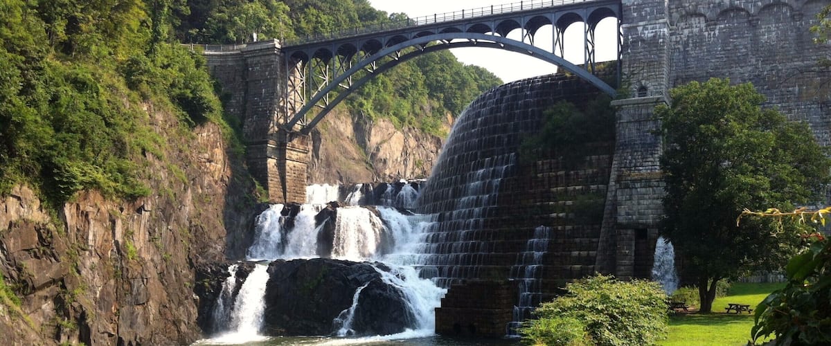A stone bridge over a river with multiple waterfalls, surrounded by lush greenery and a picnic area.